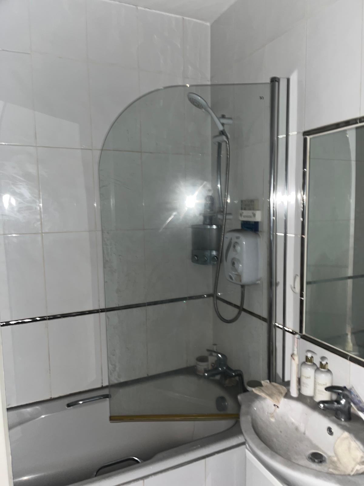 Bathroom before: white wall tiles, bath with shower screen and old basin
