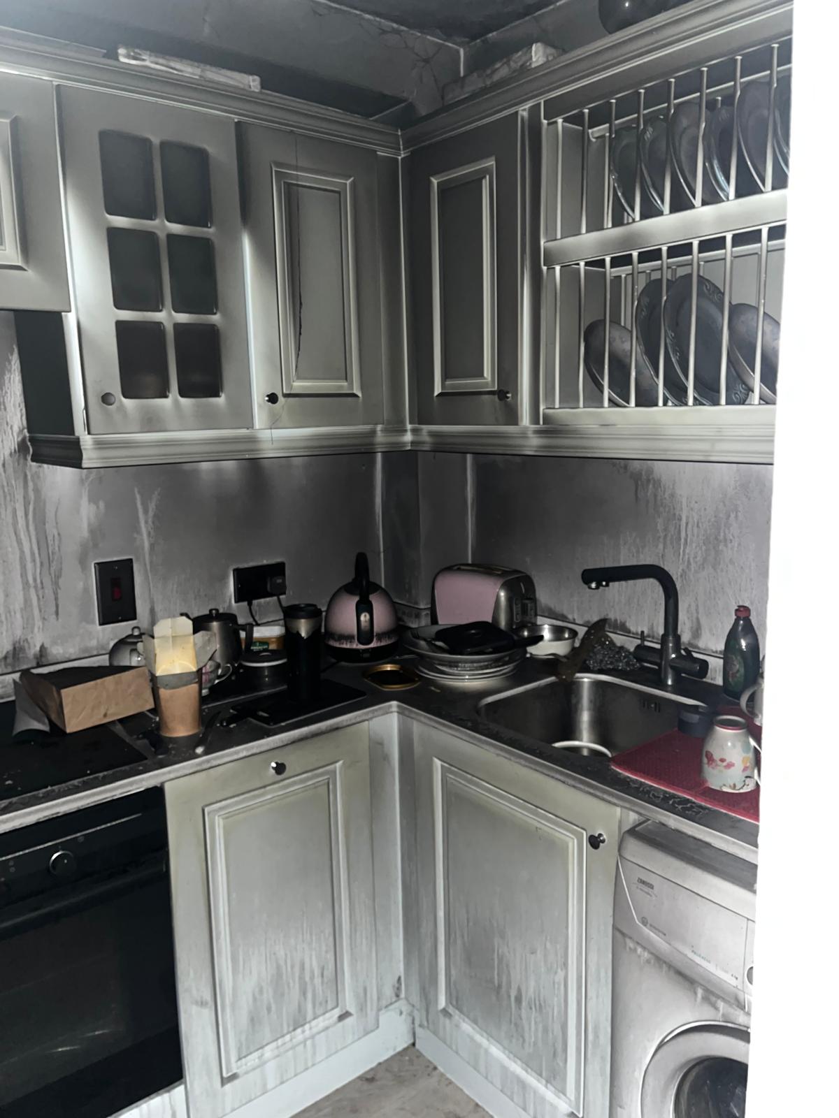 Kitchen after the fire: smoke-blackened cupboards and walls, hob, oven and sink in an L-shaped corner