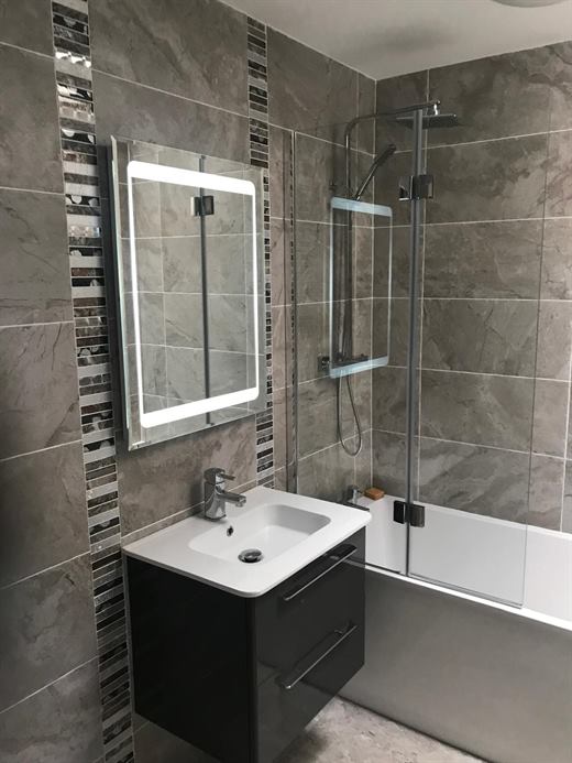 Bathroom refit with large grey tiles, LED mirror, wall-hung vanity and bath screen