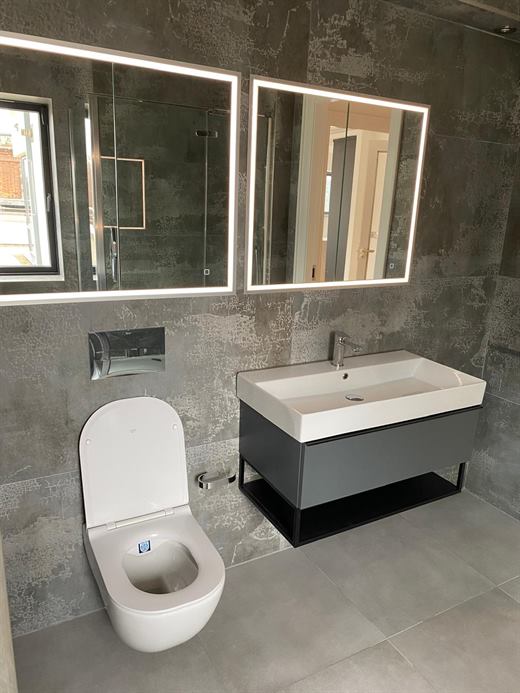 Bathroom with backlit mirrors, dark tiles and wall-hung basin
