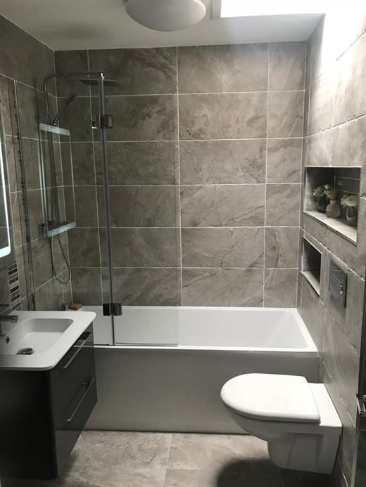 Bathroom with bath, wall-hung toilet and grey tiles