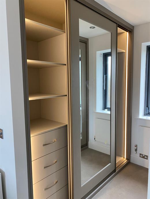 Fitted wardrobe with lit shelving and mirrored sliding door