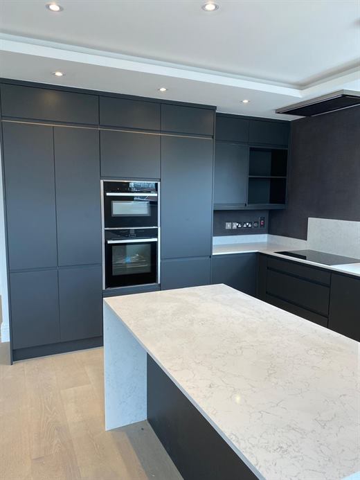 Kitchen fitted with dark handleless units, double oven and a quartz island