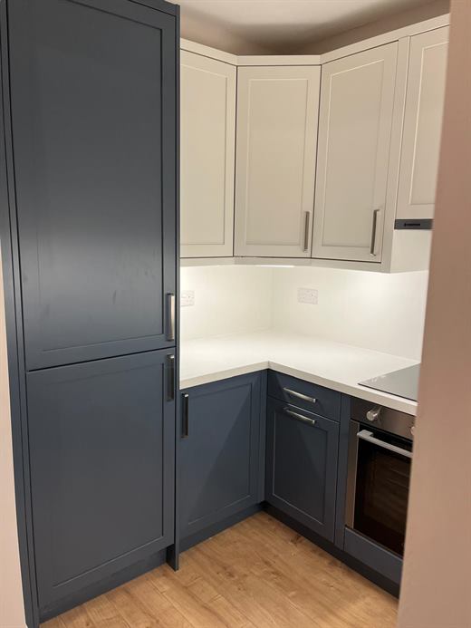Kitchen with tall navy unit, cream wall units and white worktop