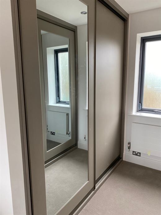 Mirrored sliding wardrobe door beside a window