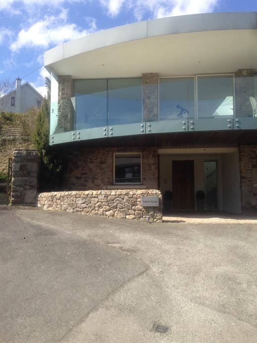 Modern two-storey house with a curved roof, glass balustrade and stone walls
