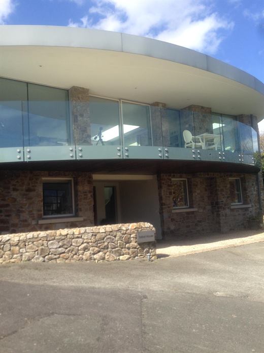 Rear of a modern house with curved roof, glass balustrade and stone walls