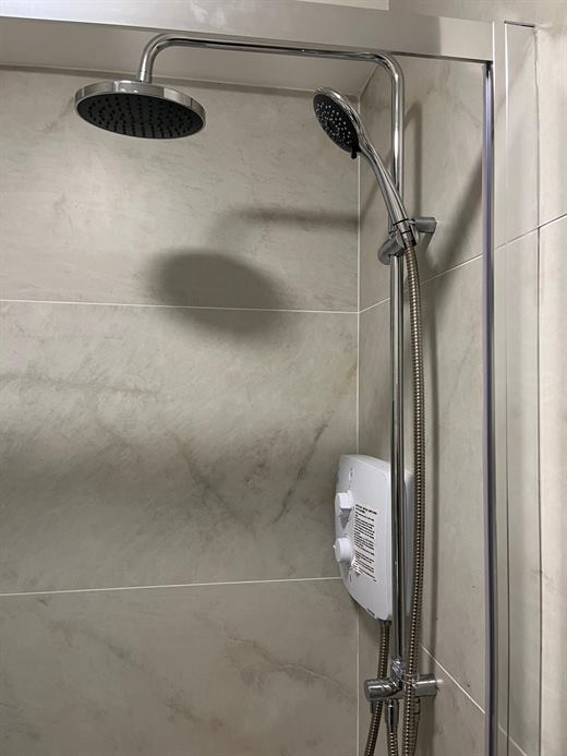 Shower with rain head and handset over marble-effect tiles