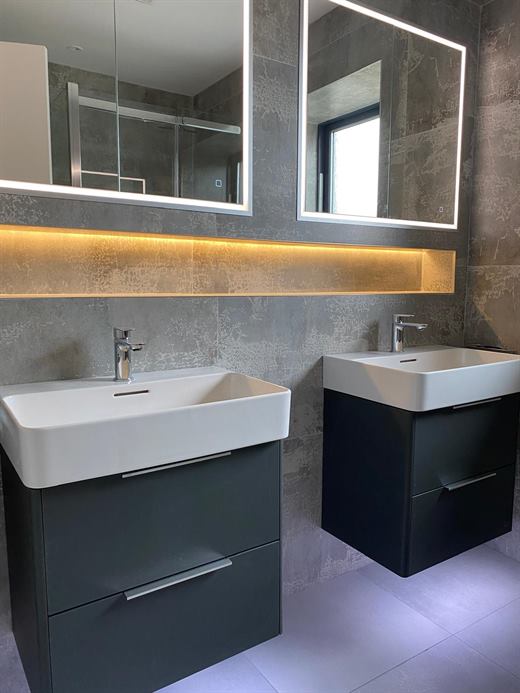 Twin basins with lit mirror cabinet and dark tiles